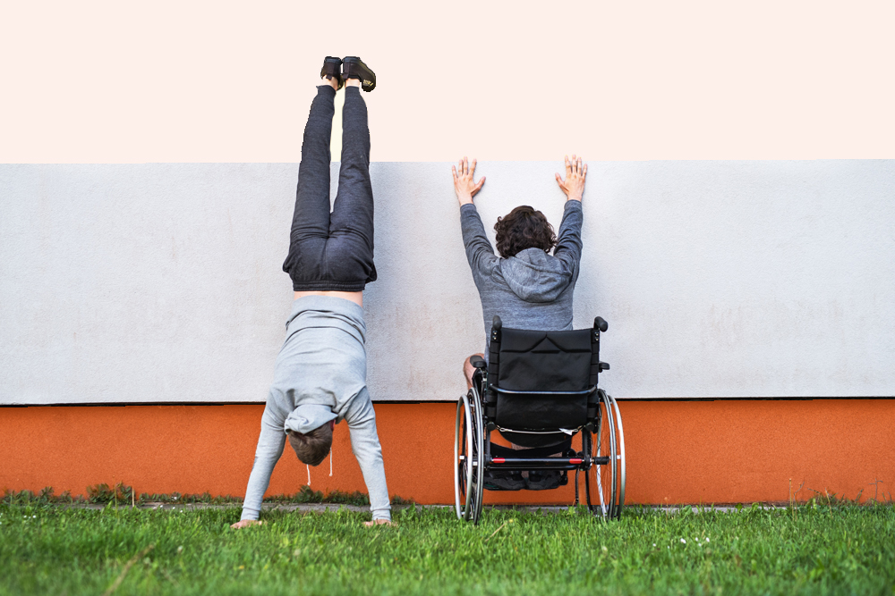 En person i rullstol håller upp händer och en person står på händer